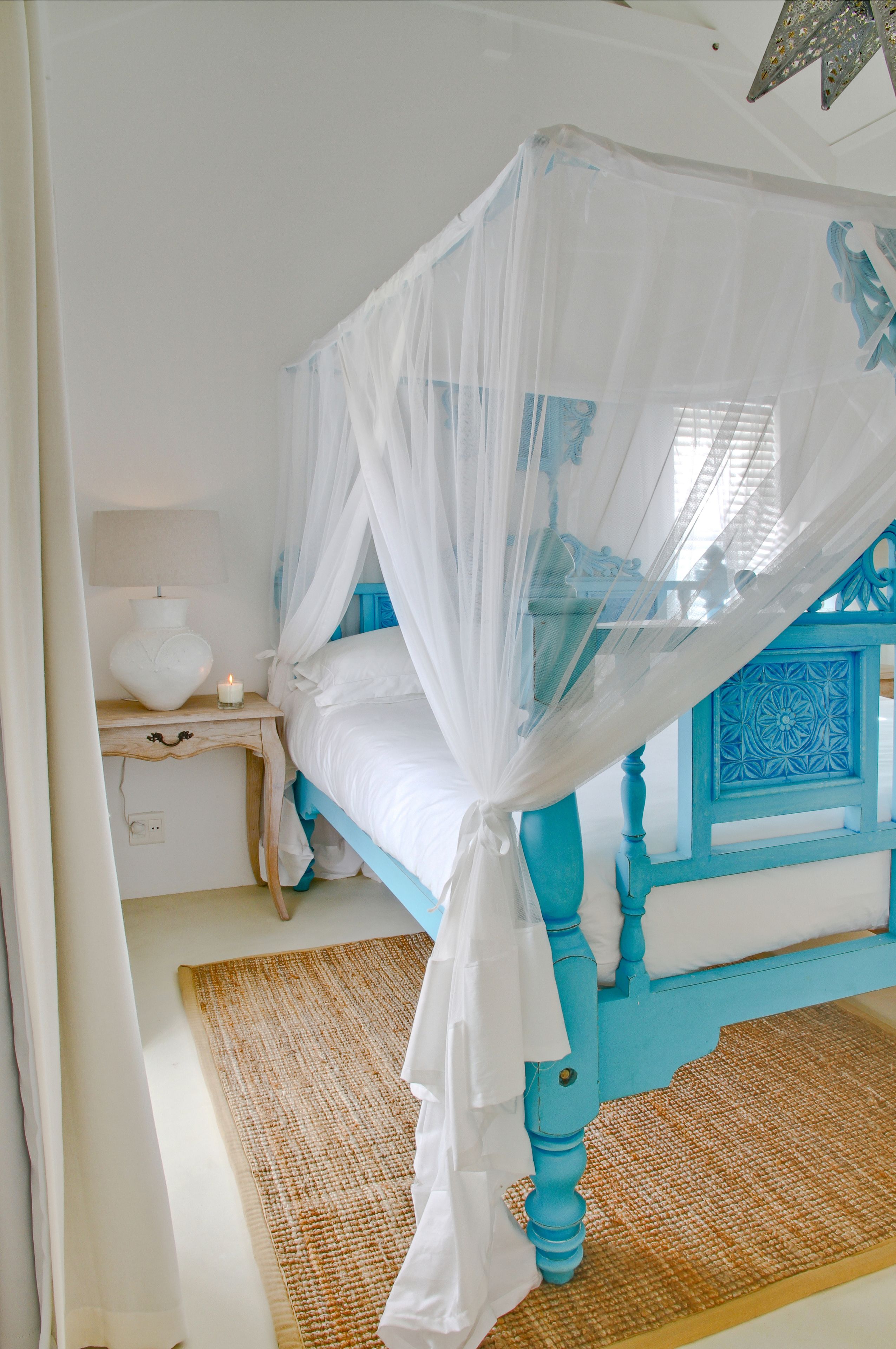 A bedroom with a four-poster bed, a nightstand, a lamp, and a decorative ceiling light.