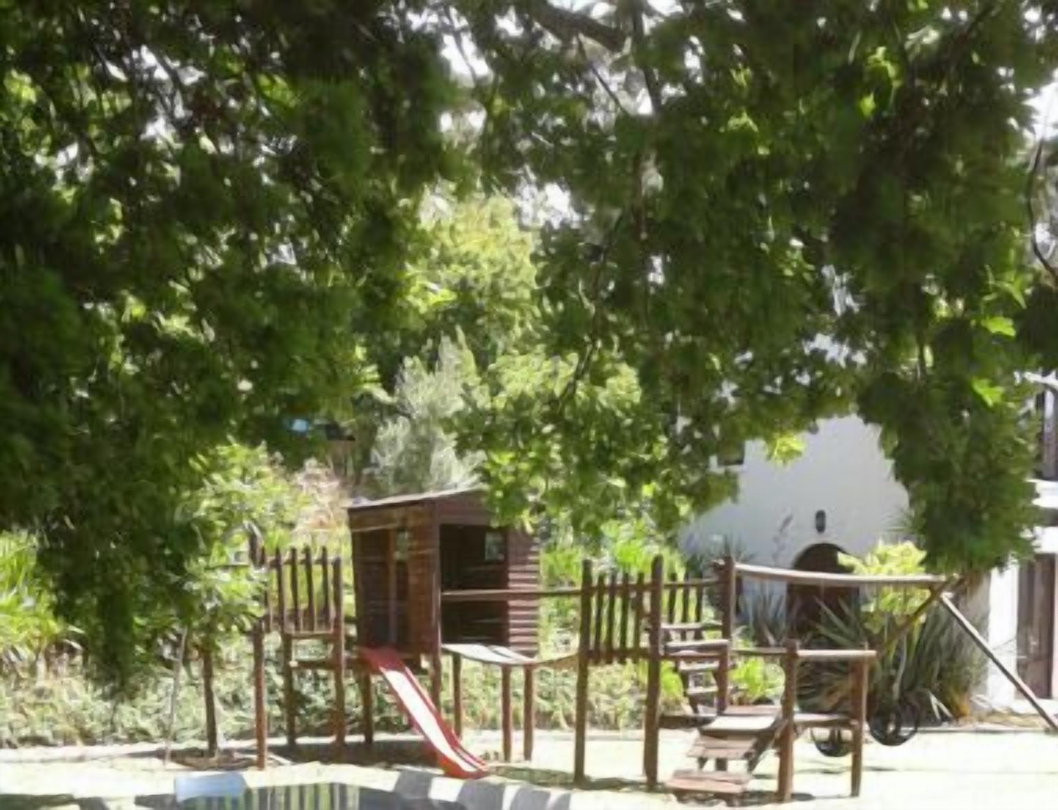 A playground with a slide and climbing structures, surrounded by trees.