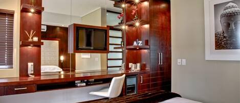 A modern bedroom with a large bed, a built-in TV, a wooden vanity, and a large mirror.