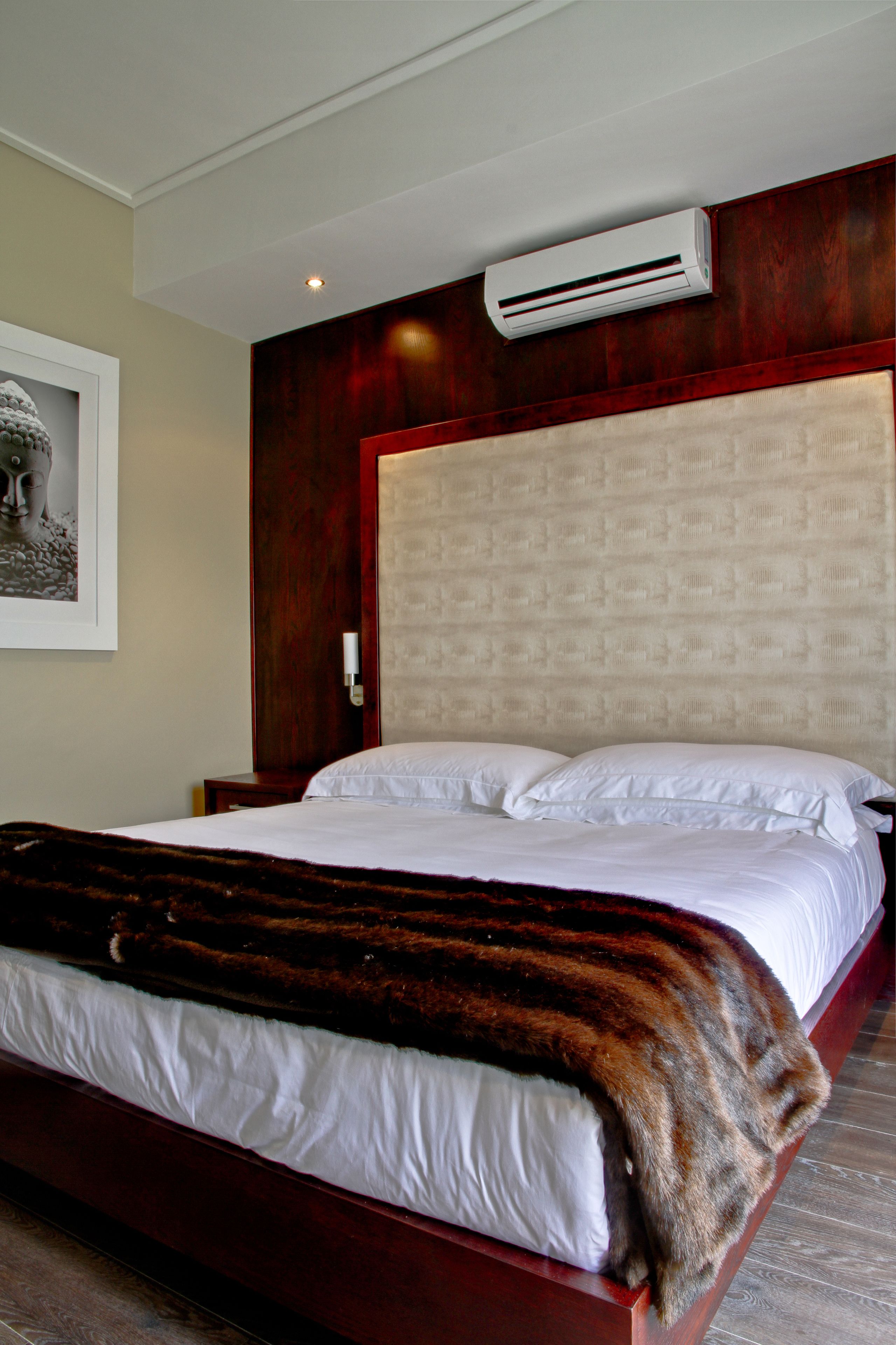 A hotel room with a large bed, a wooden headboard, an air conditioning unit, and a framed picture on the wall.
