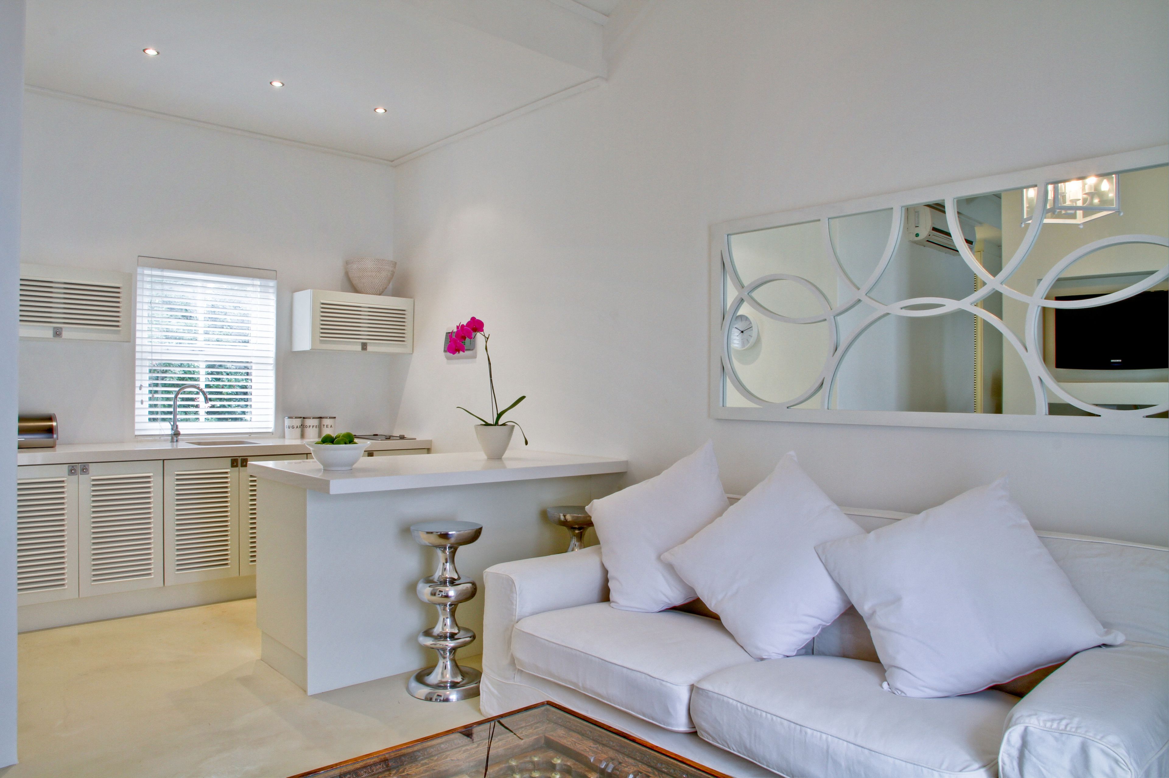 A modern, white-themed living room with a white sofa, a glass coffee table, and a decorative mirror.