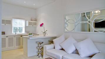 A modern, white-themed living room with a white sofa, a glass coffee table, and a decorative mirror.