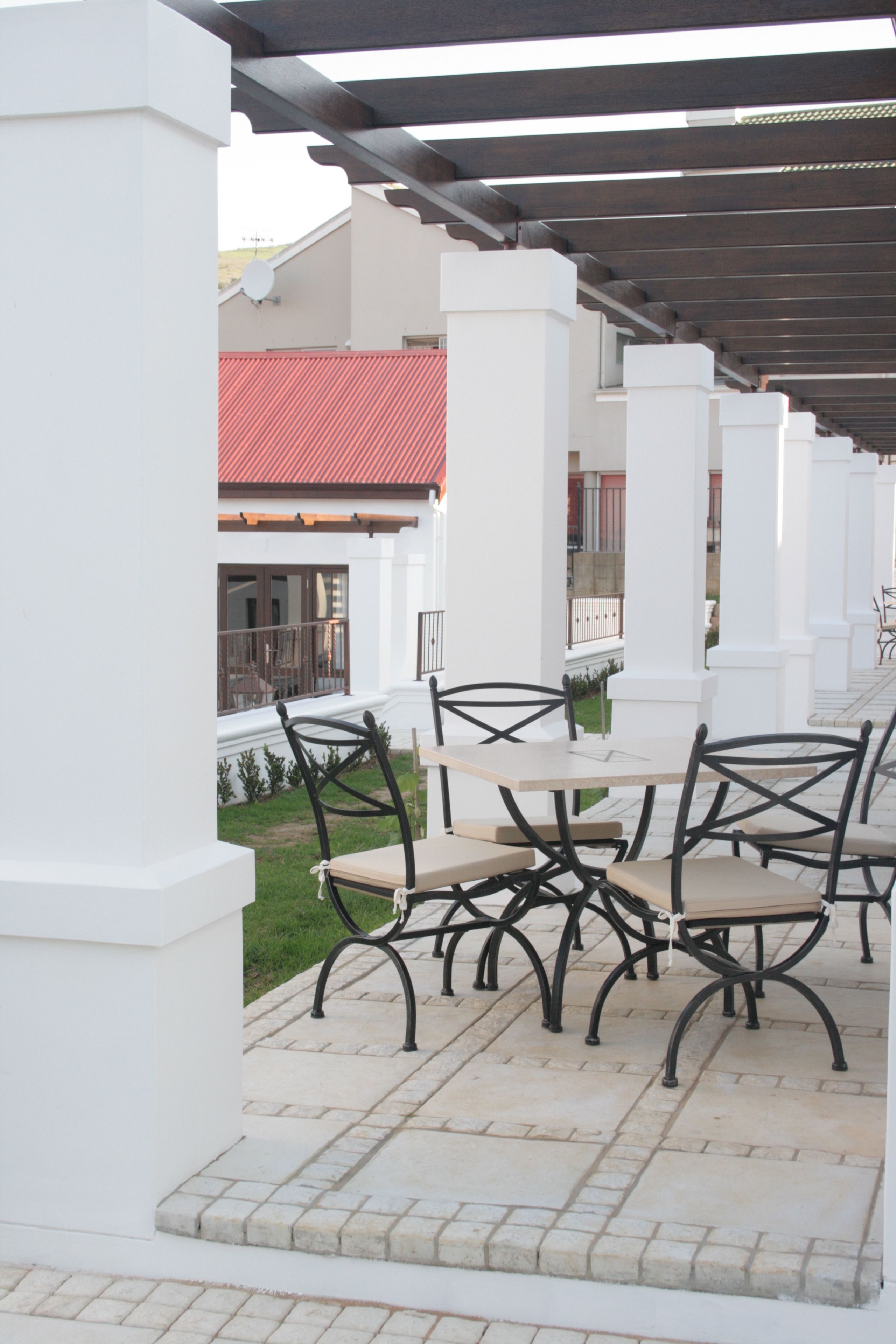 Une terrasse extérieure dotée d’une pergola, de colonnes blanches et d’une table avec des chaises.