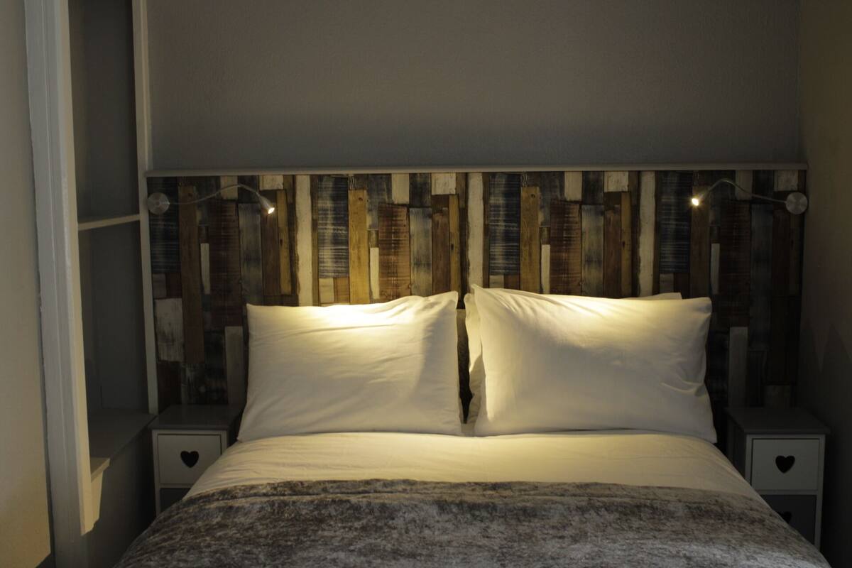 Un dormitorio con una cama, dos mesitas de noche y un cabecero con listones de madera verticales.