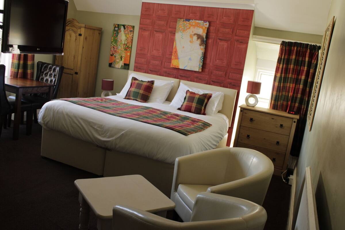 Una habitación de hotel con una cama grande, un escritorio, una silla, un aparador y dos cuadros en la pared.