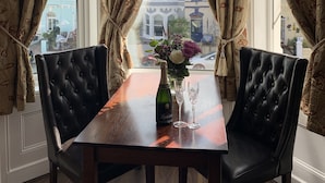 Una habitación de esquina con una mesa y dos sillas, una botella de champán y un jarrón de flores.