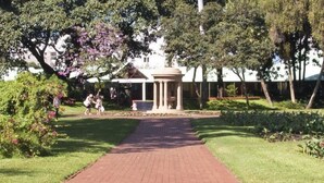 A pathway leading to a classical-style pavilion surrounded by well-maintained lawns and trees. - Coweys Corner (Durban)