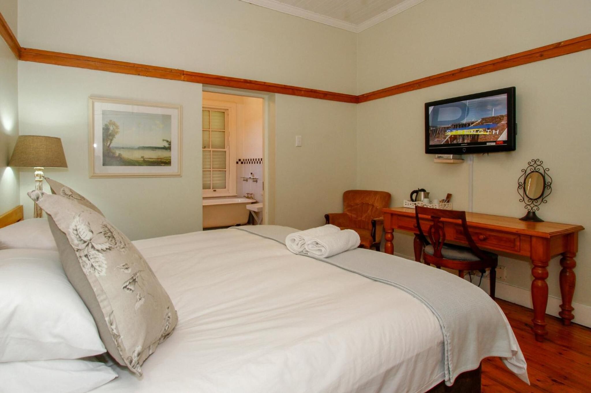 A bedroom with a bed, a desk, a chair, a television, and a framed picture on the wall.