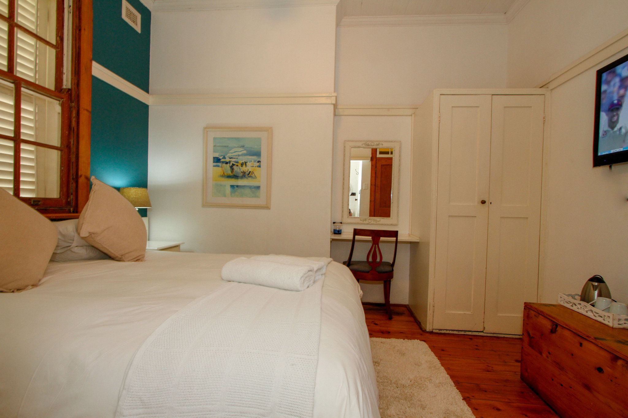 A bedroom with a bed, a desk, a chair, a wardrobe, and a television.