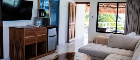 A modern living room with a flat-screen TV, wooden furniture, a sofa, and a view of a balcony with a thatched roof.
