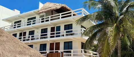 Un hotel de varios pisos con balcones, techo de paja y palmeras.