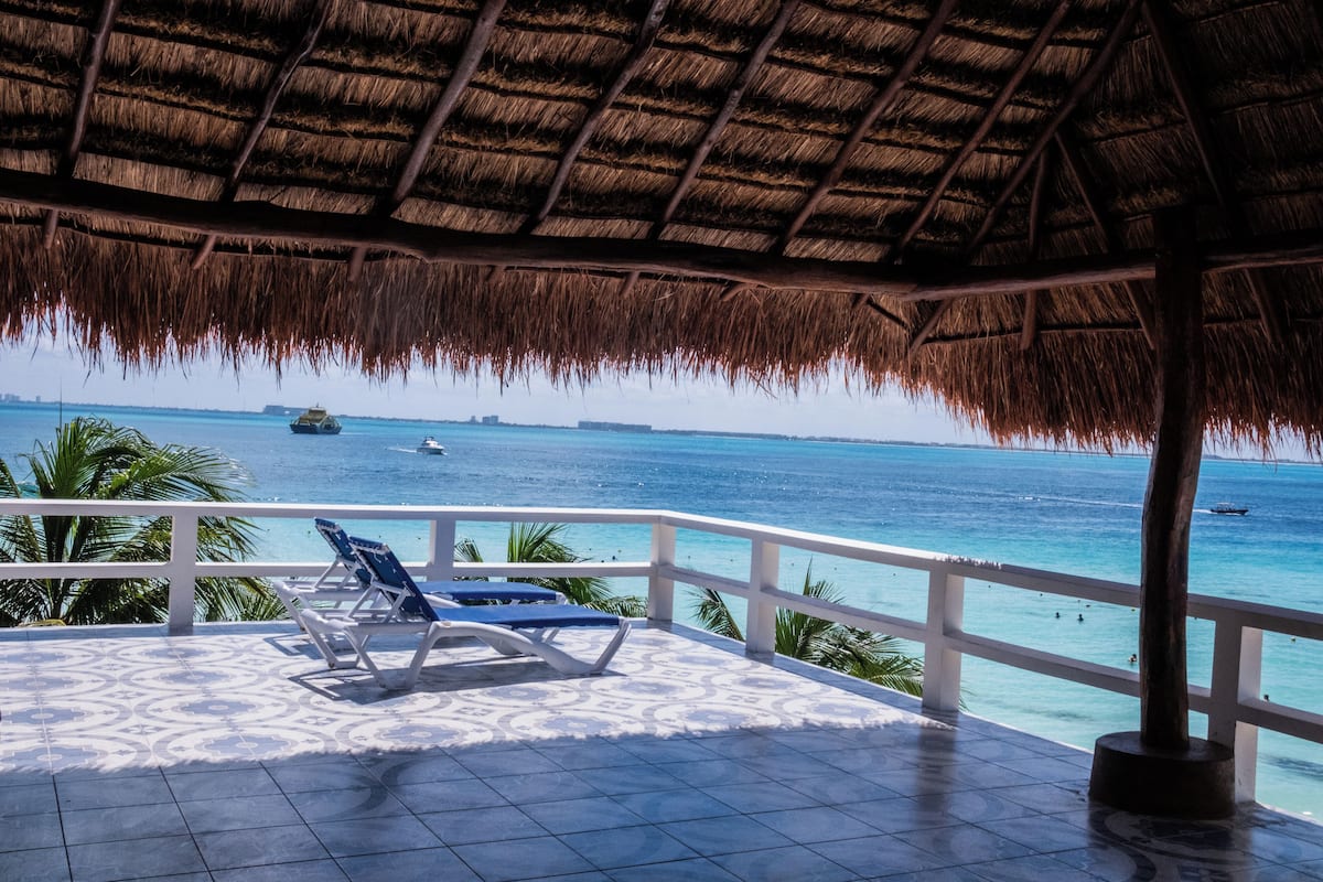 A covered outdoor area with a thatched roof, a tiled floor, and a view of the ocean.