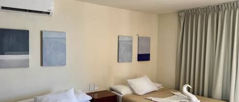 Una habitación de hotel con dos camas, ropa de cama color beige, toallas blancas y obras de arte en las paredes.