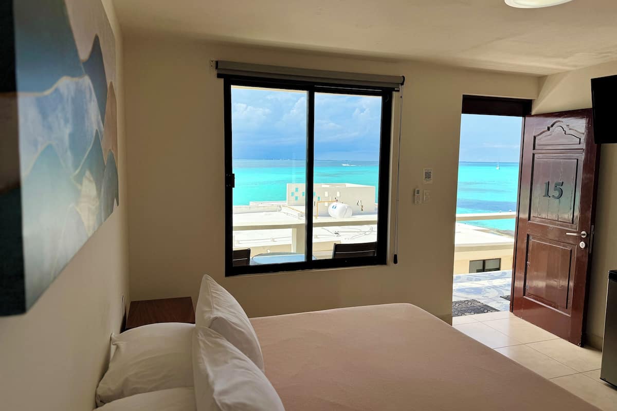 A bedroom with a large window offering a view of the beach and ocean.