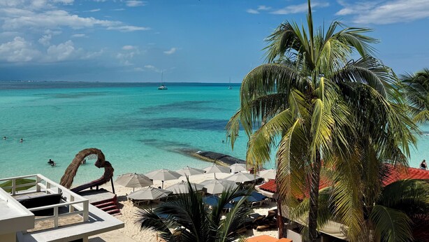 Una playa con agua turquesa cristalina, un velero y una palmera.