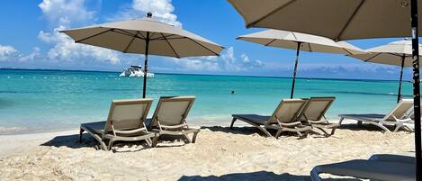 A beach with sun loungers and umbrellas, a boat in the water, and clear turquoise sea.