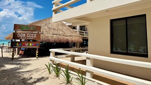 Un edificio frente a la playa con techo de paja, un letrero que dice 'Don Cuco Beach Lounge' y un letrero que dice 'Isla Mujeres México'.