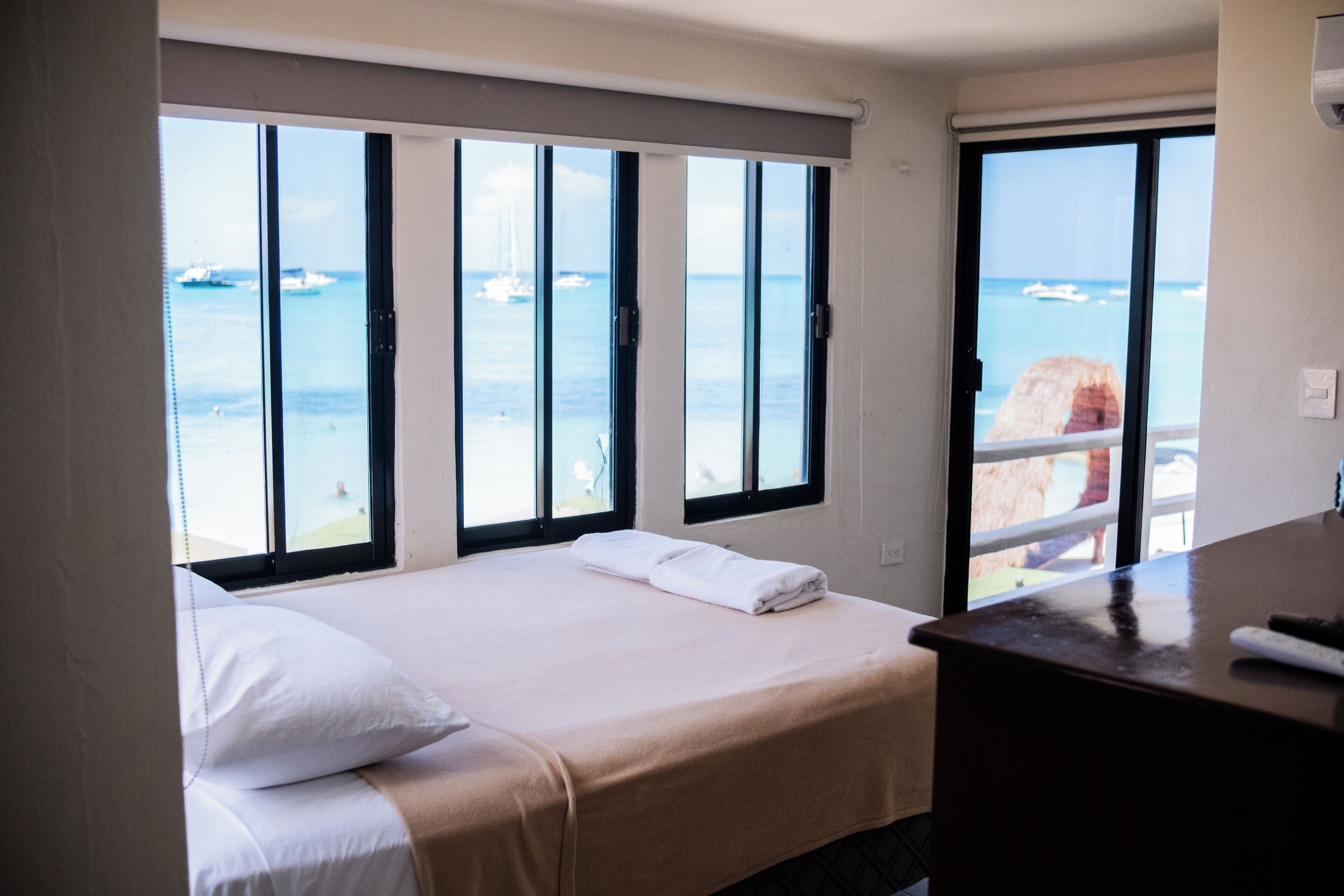 A hotel room with a bed, a desk, and a view of the ocean through large windows.