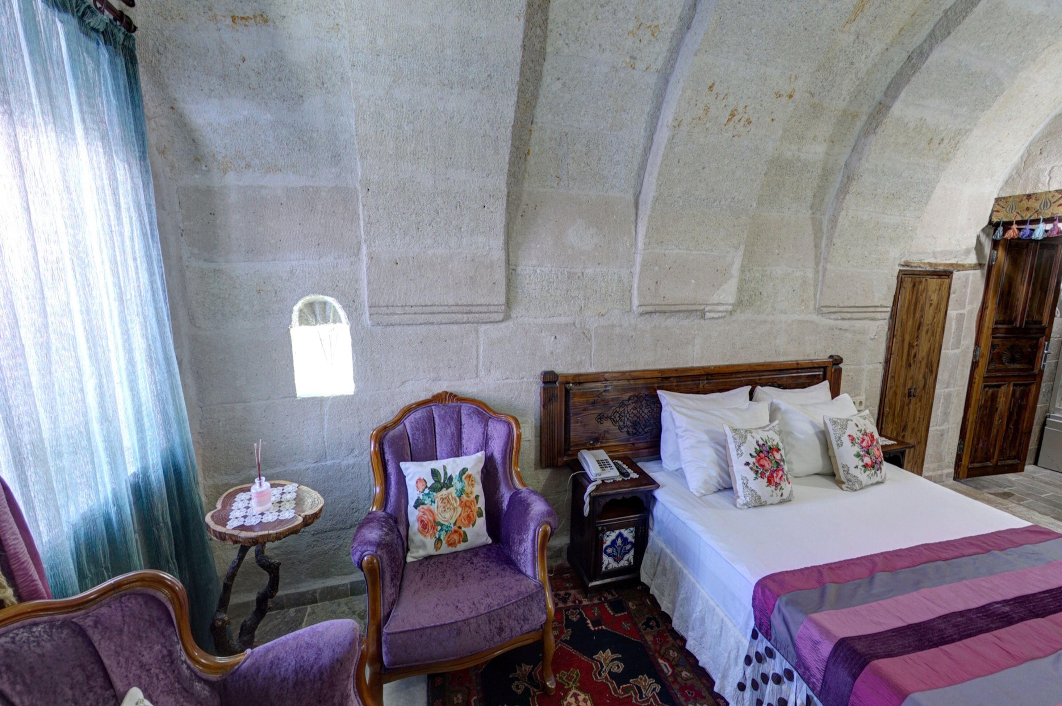 A room with a bed, a chair, a small table with a candle, and a window with a curtain.