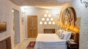 A bedroom with a large bed, a wooden wardrobe, a decorative wall, and a patterned rug. - Roc Of Cappadocia (Nevsehir)