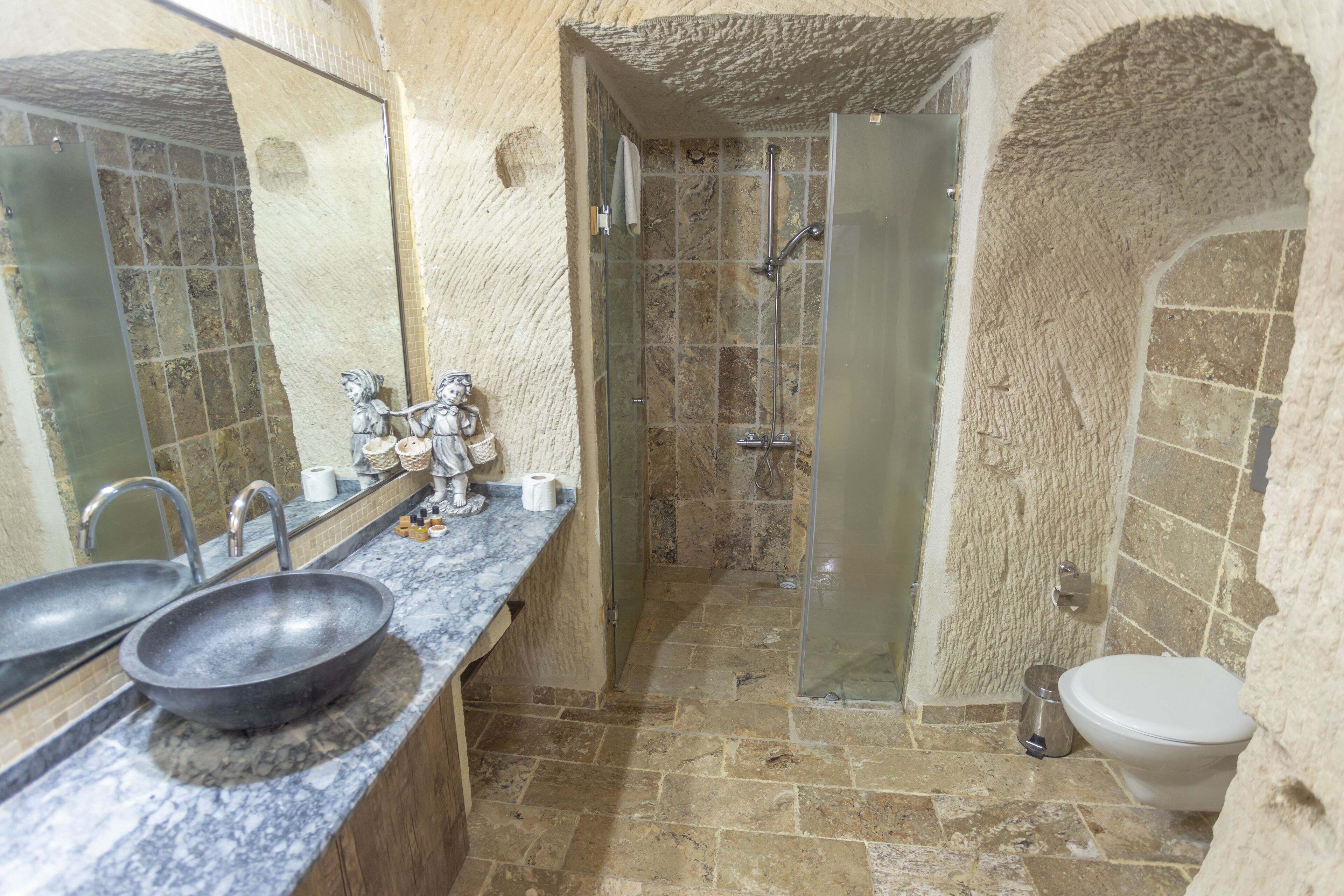 A bathroom with a large mirror, two sinks, a shower, and a toilet.