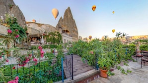 A rooftop garden with potted plants and a wooden deck, overlooking a mountainous landscape with hot air balloons in the sky. - Roc Of Cappadocia (Nevsehir)