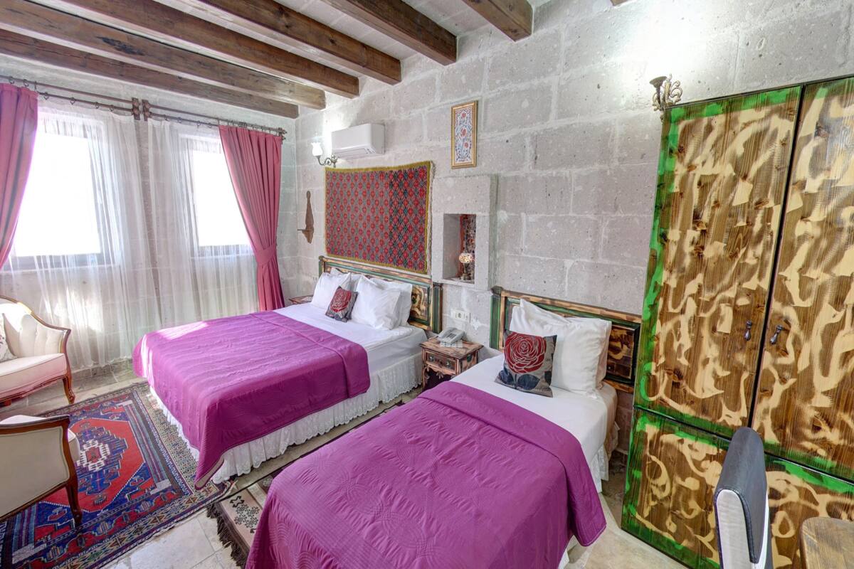 A room with two beds, a chair, a rug, a wooden wardrobe, and a wall-mounted telephone.