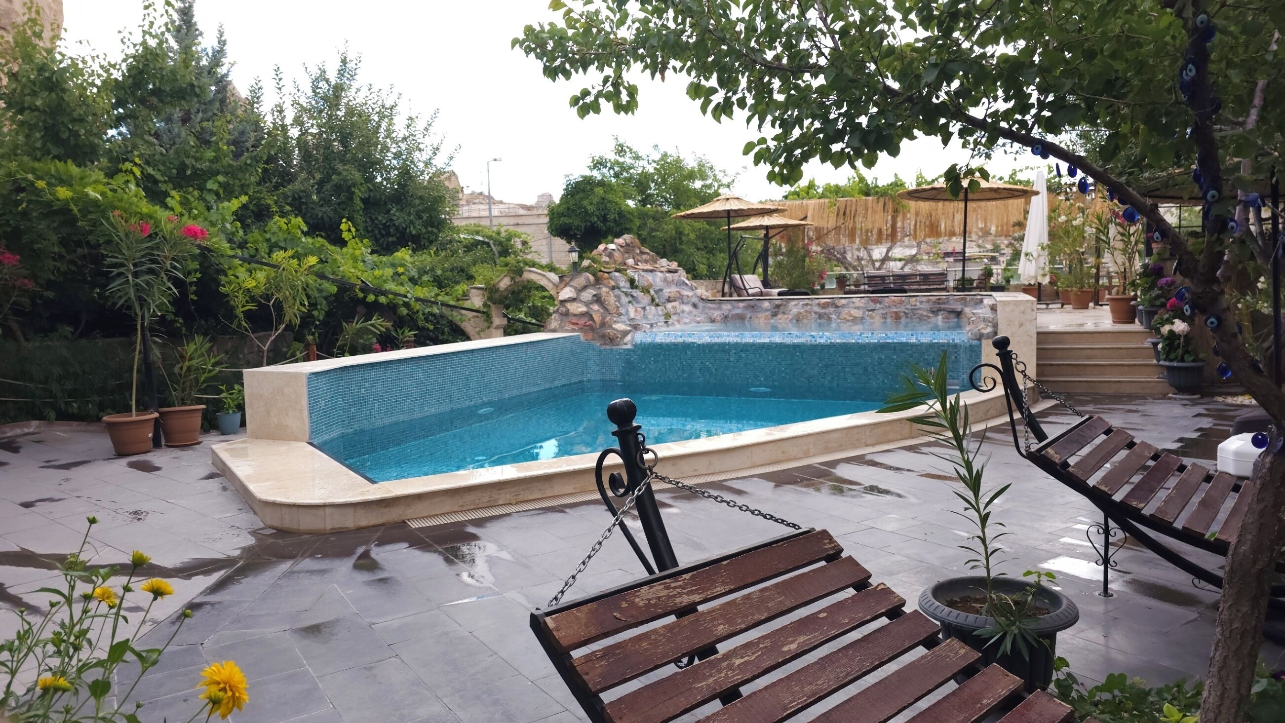 A swimming pool with a tiled edge, surrounded by potted plants and a wooden bench.