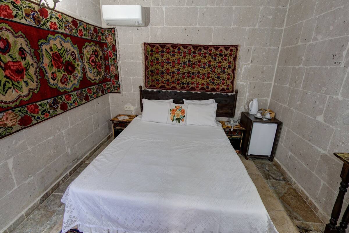 A room with a bed, a nightstand, a small refrigerator, and a wall-mounted air conditioner.