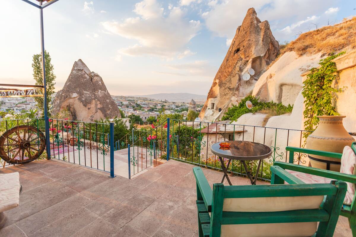 A terrace with a view of a city and mountains, featuring a table, chairs, and a decorative wheel.