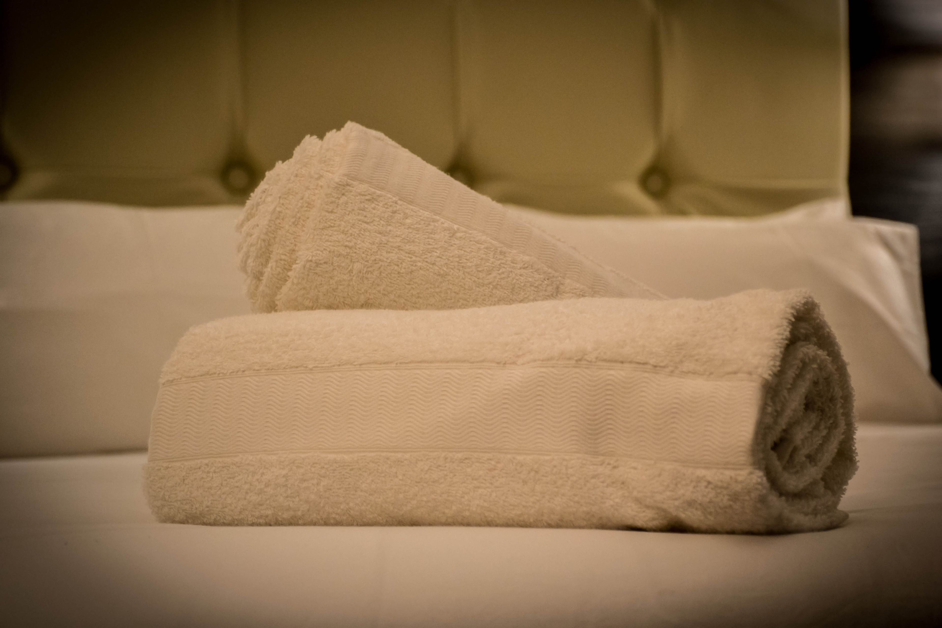 A neatly made bed with a rolled-up white towel and a folded white towel.