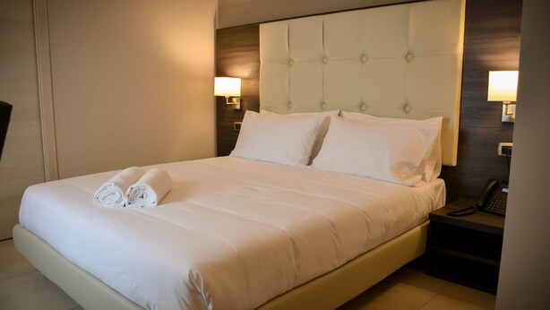A hotel room with a large bed, two bedside lamps, and a nightstand with a phone. - Brain Rooms & Suite (Pagani)