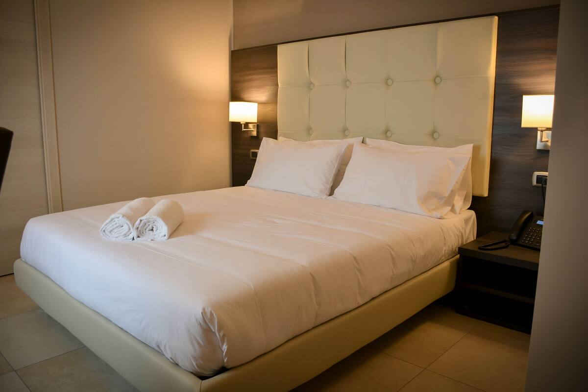 A hotel room with a large bed, two bedside lamps, and a nightstand with a phone.