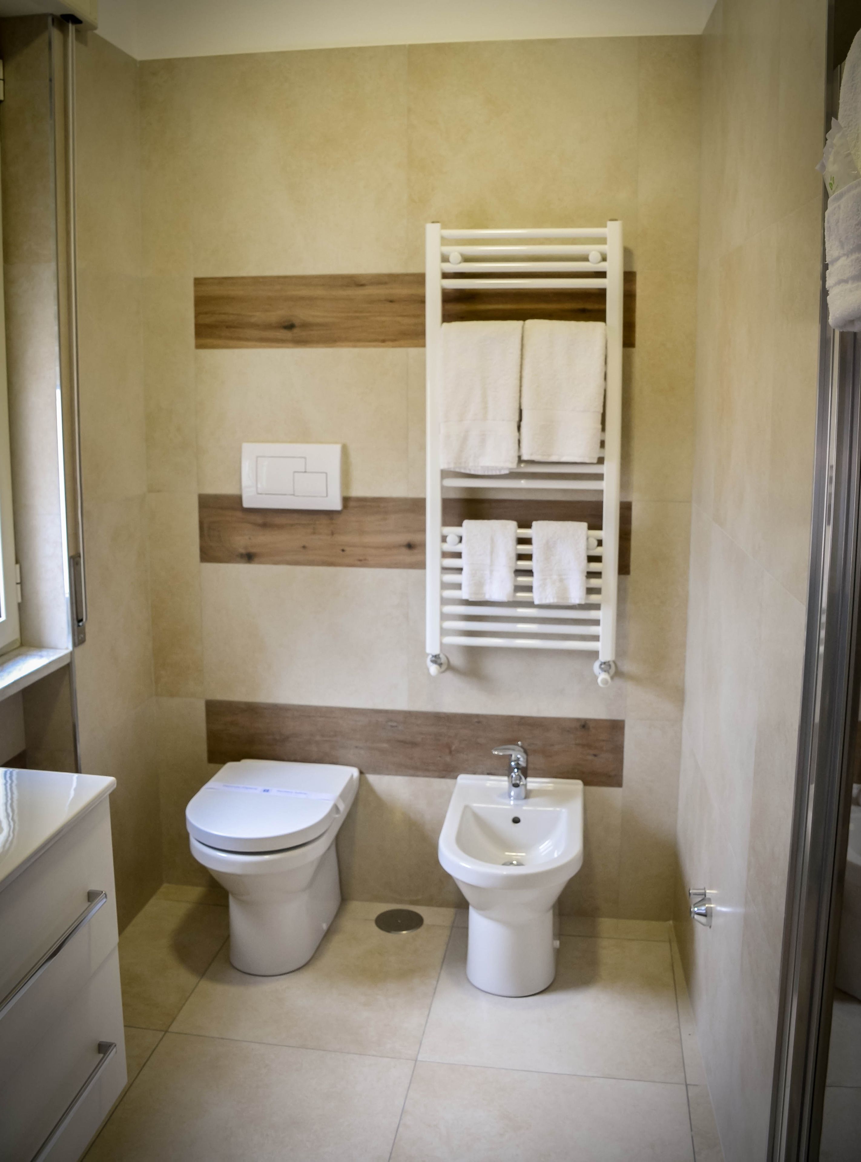 Et badeværelse med toilet, bidet og et håndklædetørrestativ med håndklæder.