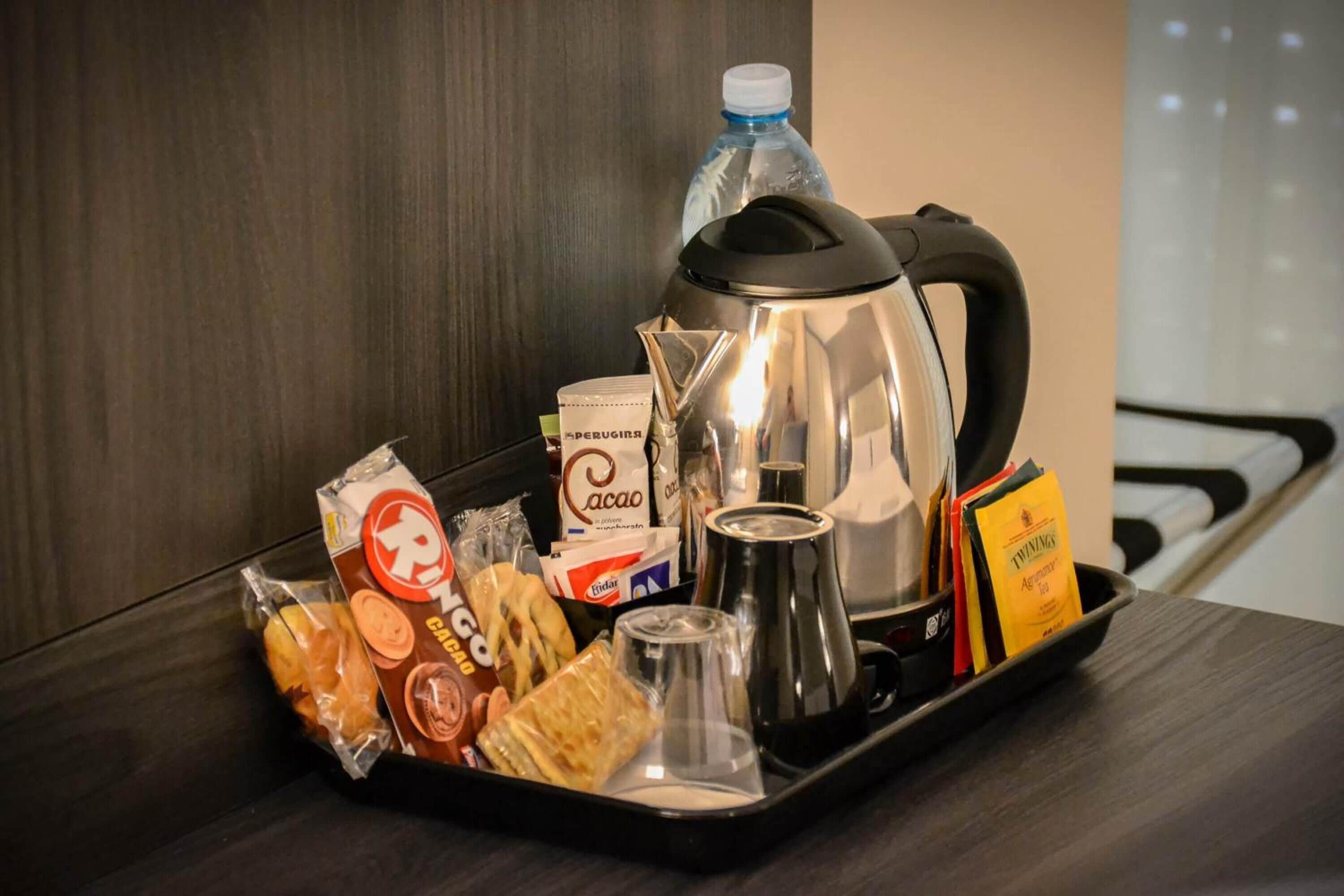 A tray with a coffee maker, a water bottle, snacks, and a glass.