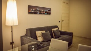 A modern living room with a grey sofa, a glass coffee table, and a cityscape painting on the wall. - Brain Rooms & Suite (Pagani)