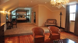 A spacious bedroom with a large bed, a sitting area with wicker chairs, a chandelier, and a view of the outside. - Kearsney Manor Guesthouse (KwaDukuza)