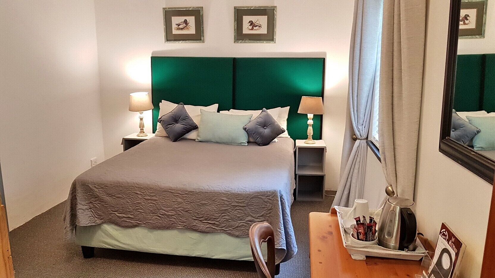 Habitación de hotel con cama, dos mesitas de noche, una silla, escritorio, espejo y cuadros en la pared.