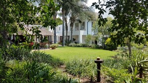 A well-maintained garden with a lawn, various plants, and a building with multiple windows and a thatched roof. - Six Valk Avenue Guest House (Sandton)