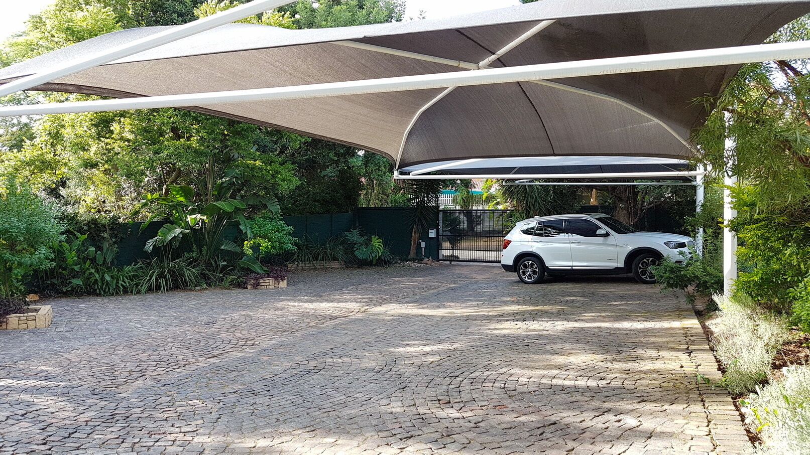 Un área de estacionamiento techada con un camino pavimentado que lleva a un coche blanco aparcado bajo una marquesina.