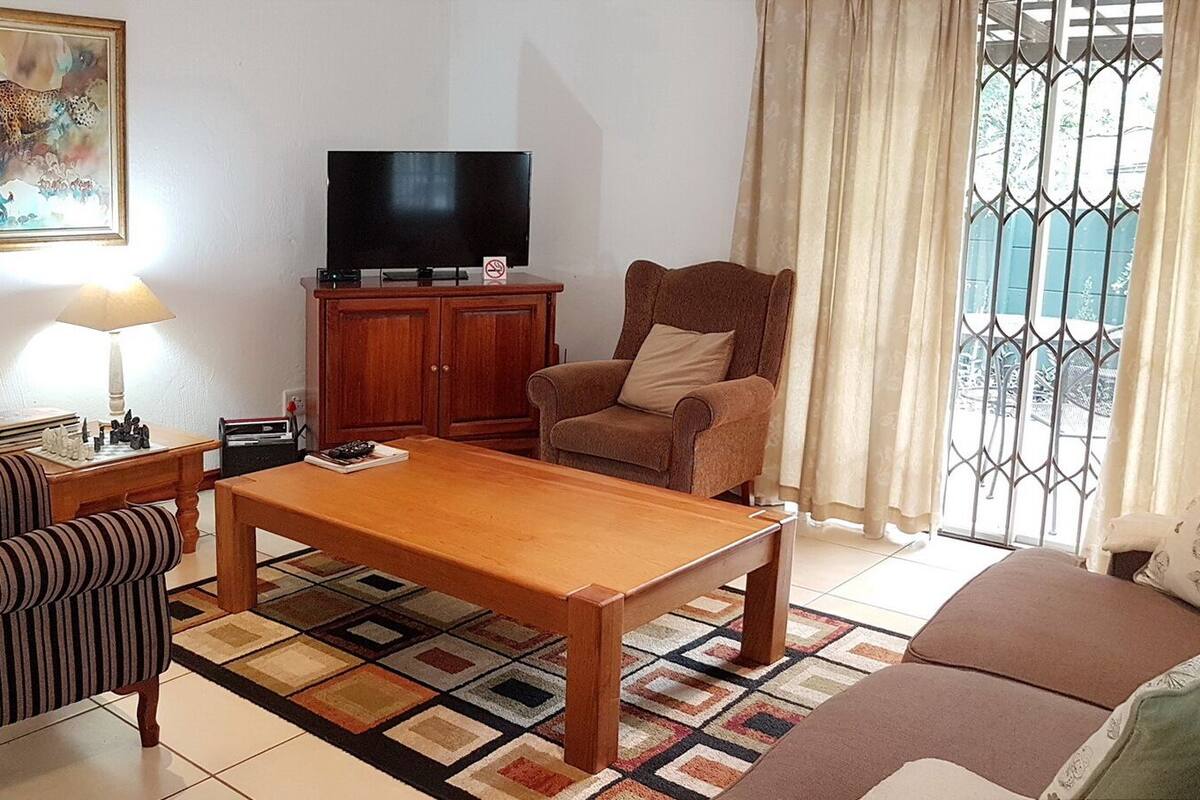 Un salon comprenant un canapé, un fauteuil à rayures, une table basse en bois, un téléviseur, un meuble et un tapis à motifs.