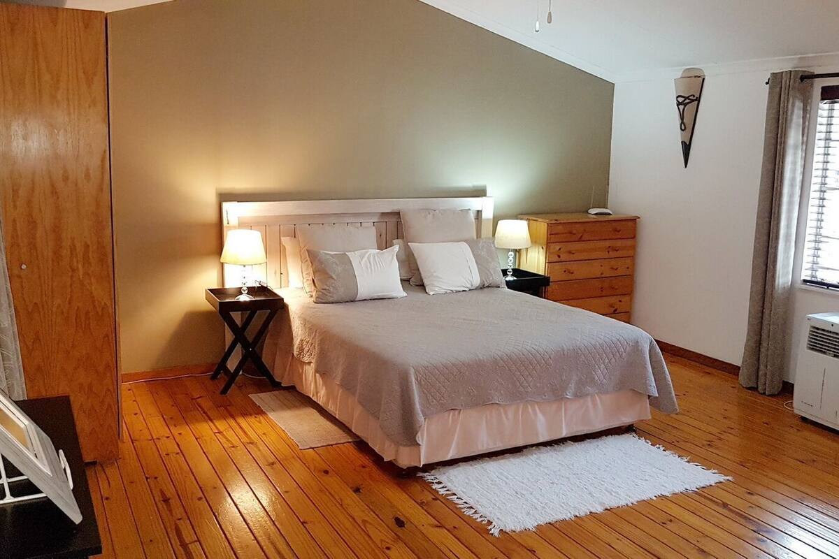 Une chambre à coucher comprenant un lit, des tables de chevet, une commode, un radiateur et une fenêtre avec des rideaux.