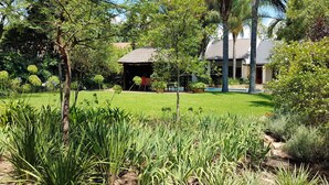 A lush garden with a gazebo, a swimming pool, and a house with a tiled roof. - Six Valk Avenue Guest House (Sandton)