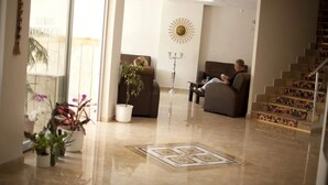 Un salon moderne avec un canapé, une table basse et une plante en pot. On aperçoit, au fond, un escalier dont les marches sont décoratives.