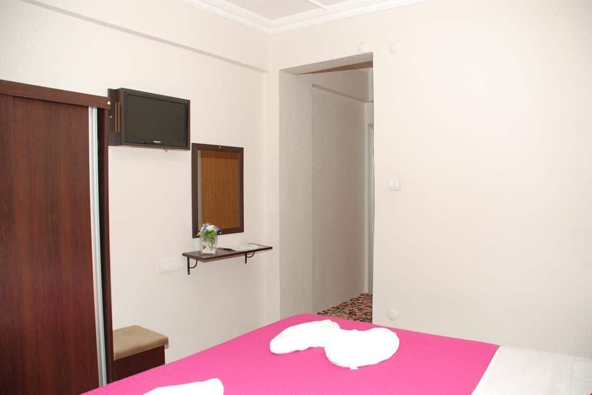 Een slaapkamer met een bed, een aan de muur bevestigde televisie, een houten garderobe en een klein plankje met een vaas.