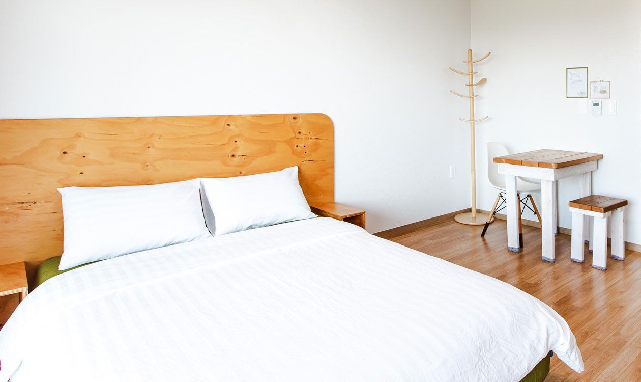 Une chambre à coucher avec une tête de lit en bois, un lit avec une literie blanche, un petit bureau en bois et une chaise.