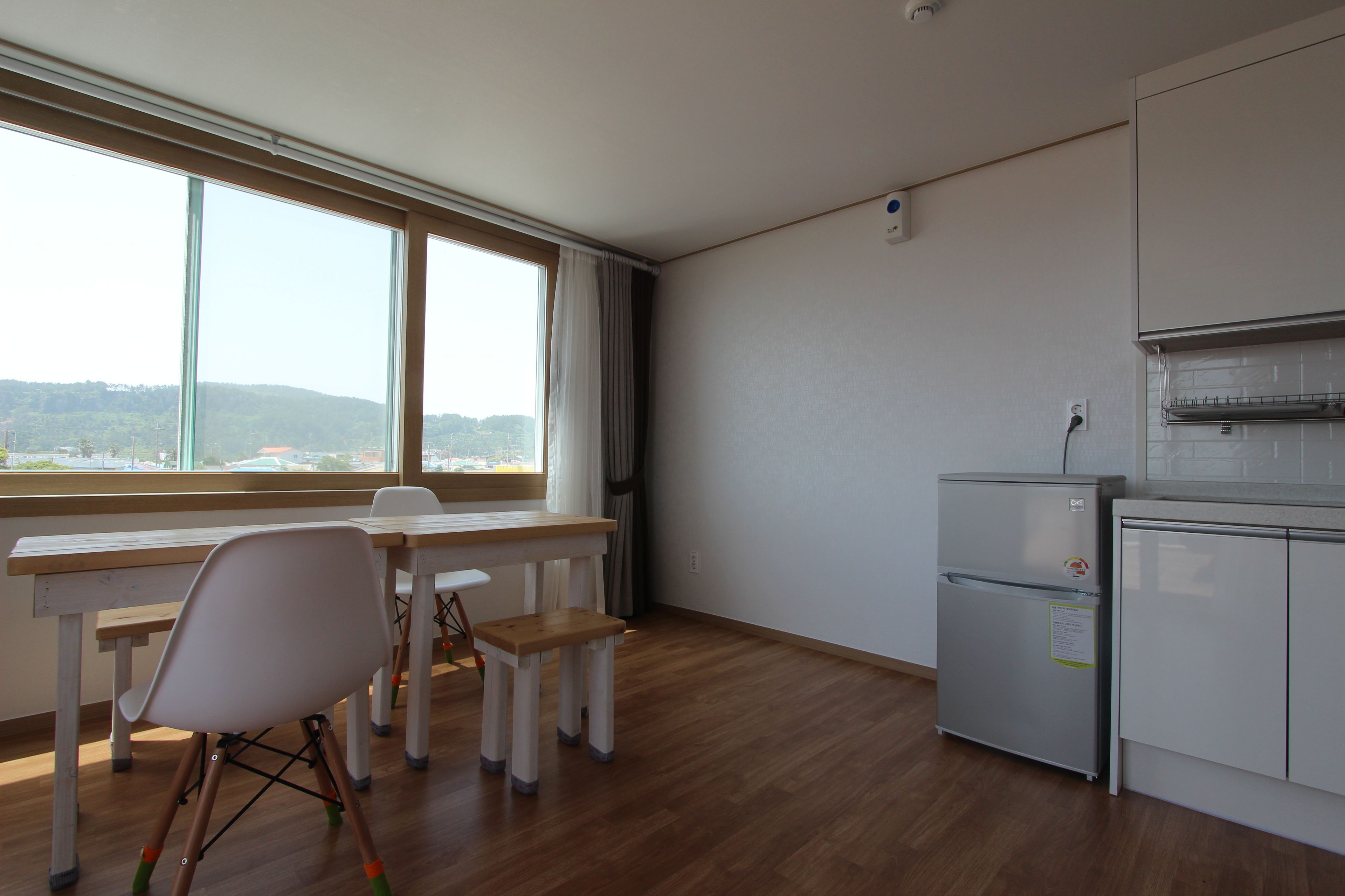 Eine Küche mit Holztisch, einem weißen Stuhl, einem Kühlschrank und einem Fenster mit Blick auf die Stadt.