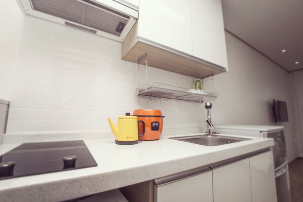Una cocina moderna con armarios blancos, un lavamanos de acero inoxidable y una encimera con un hervidor y una cafetera.