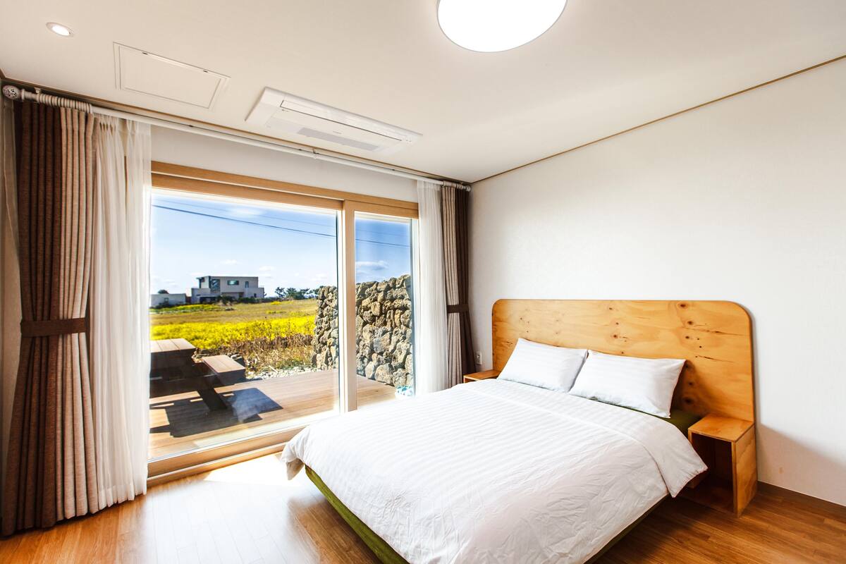 A bedroom with a large bed, wooden headboard, and a view of a field through a sliding glass door.