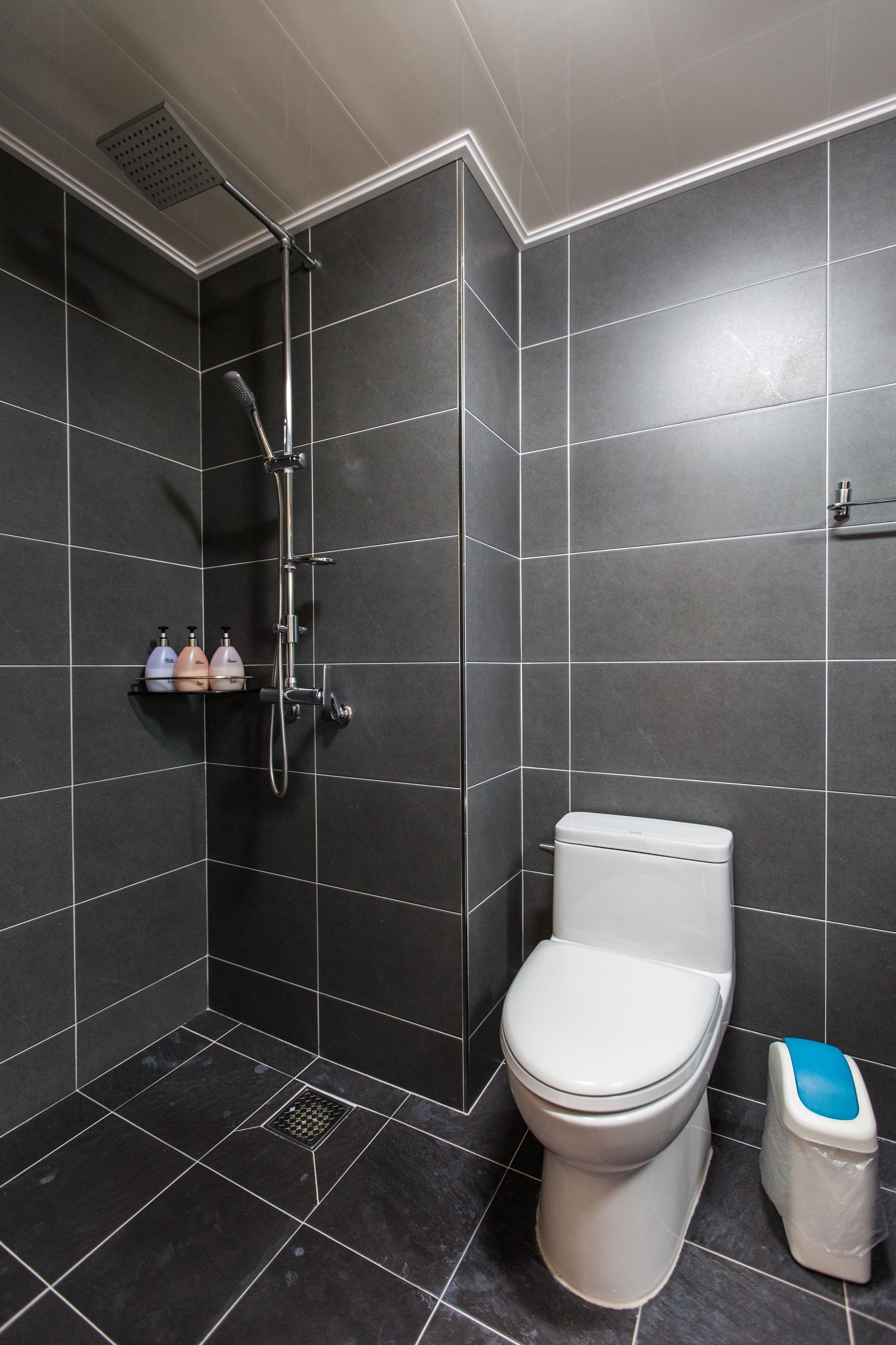 Een moderne badkamer met donkere tegels, een wit toilet, een douche en een klein plankje met toiletartikelen.